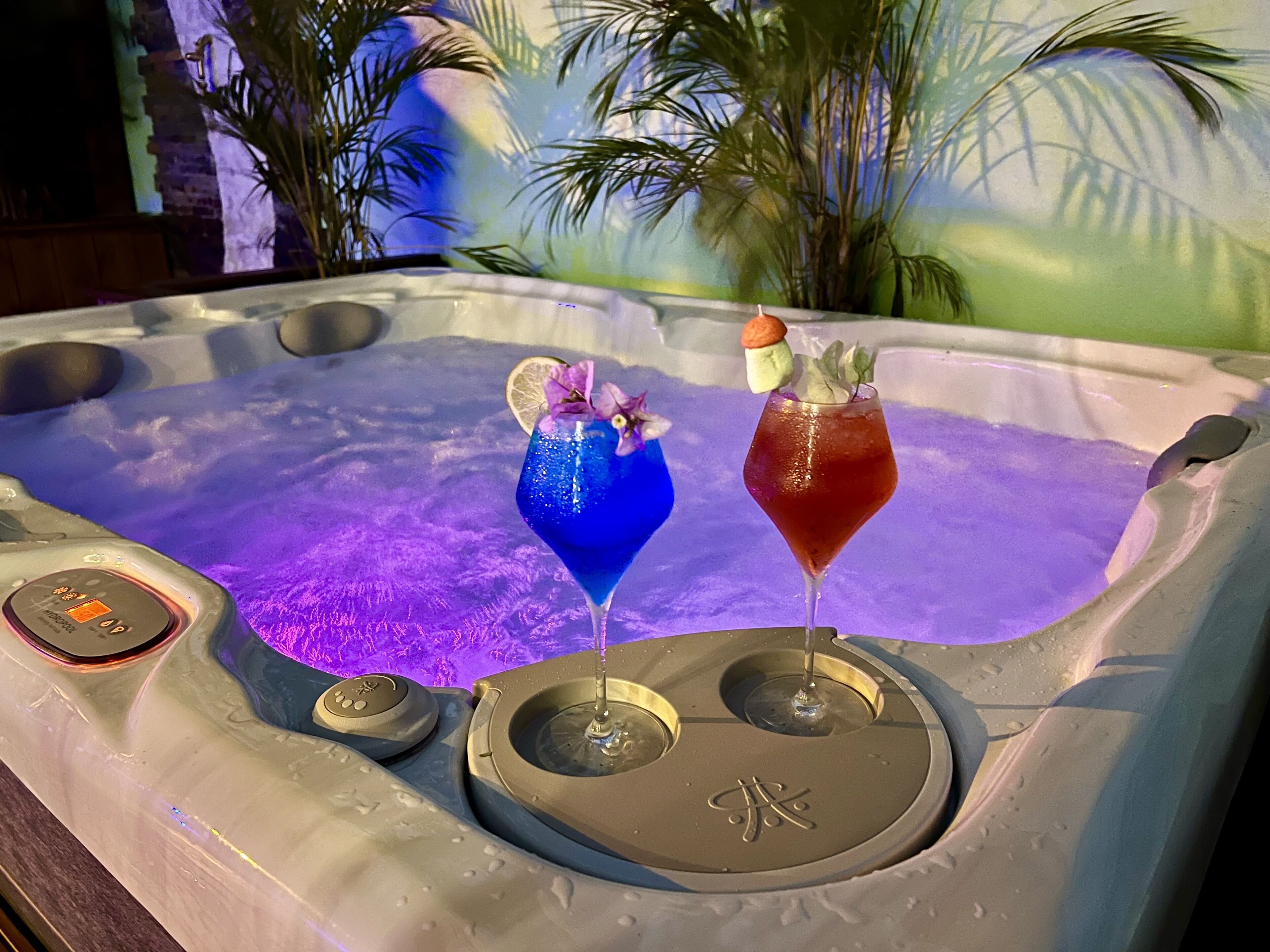 A hot tub with two drinks, one blue and one red, and a small orange object on the edge.