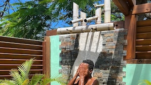 Una persona de pie bajo una ducha, con pared de piedra y vigas de madera.