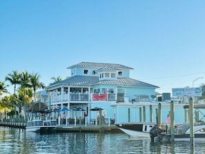 A waterfront building with a balcony, docked boats, and a sign reading "Marinas Bay". - Top Floor Beachfront & Sunset Views! Walk to Everything! Smart TVs + Workspace! (Fort Myers Beach)