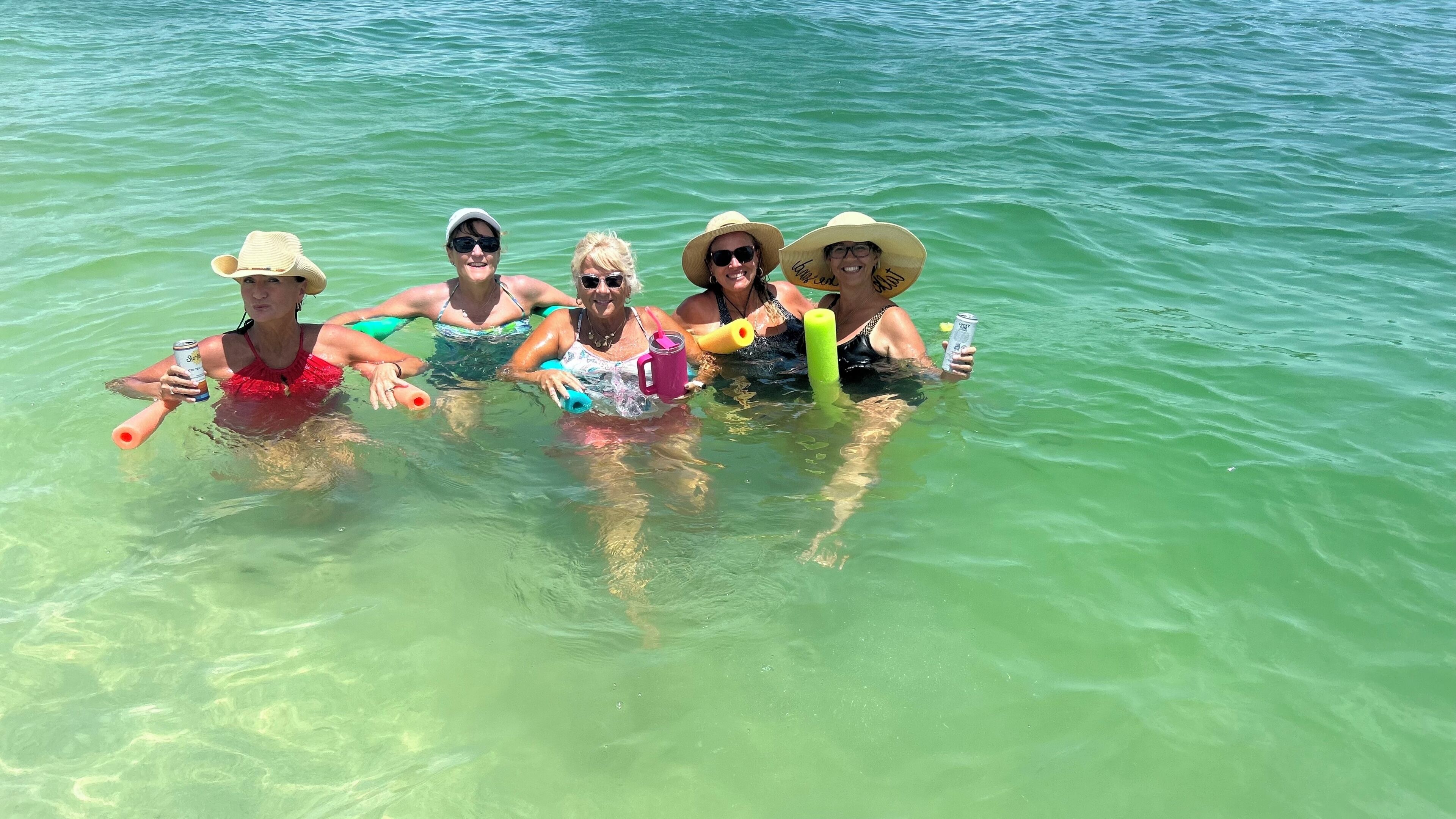 Eine Gruppe von Menschen im klaren Wasser, die Getränke und Schwimmhilfen halten.