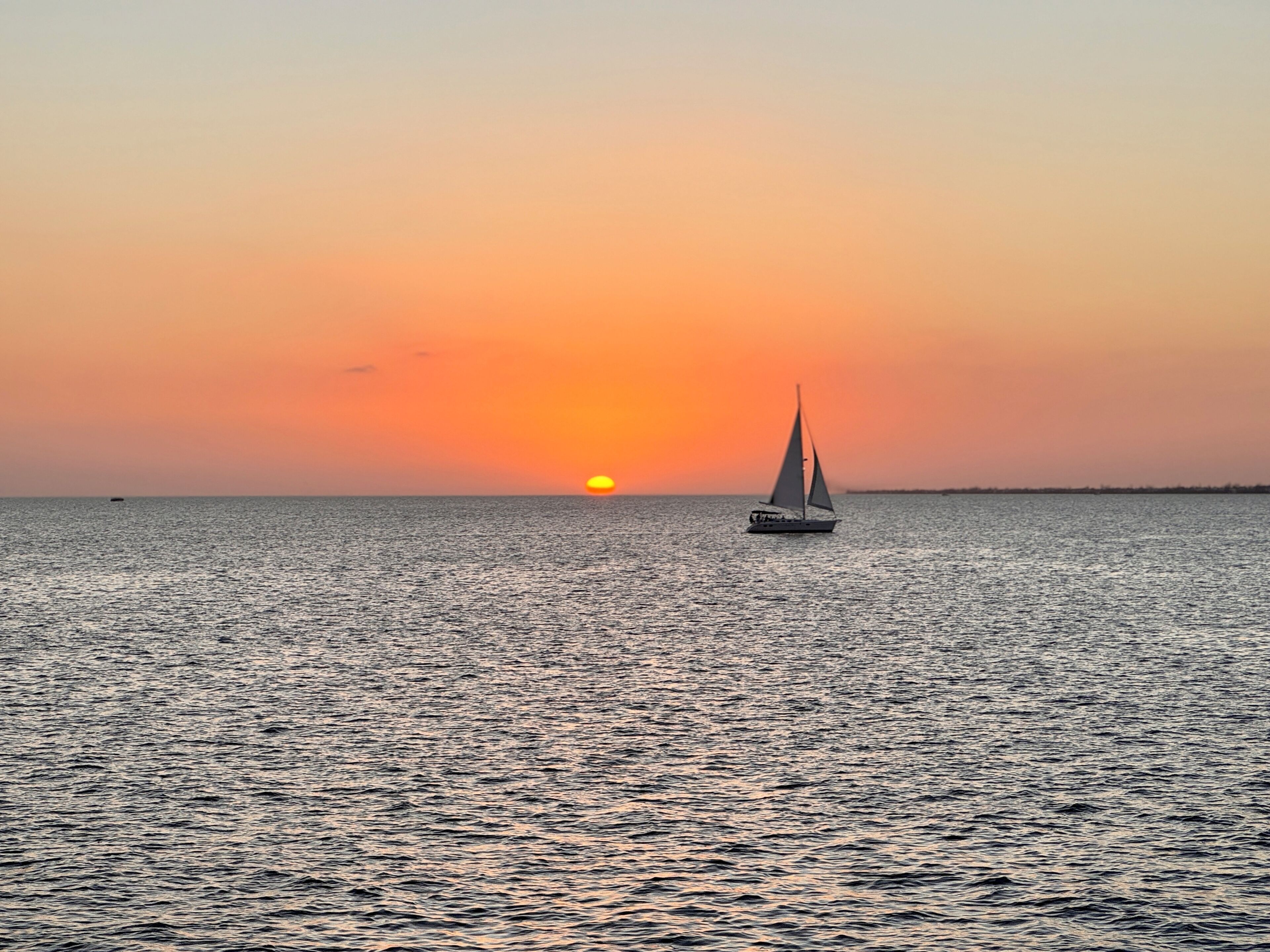 Een zeilboot op rustig water met een zonsondergang op de achtergrond.