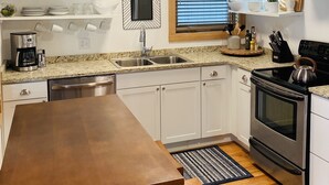 A modern kitchen with white cabinets, a granite countertop, stainless steel appliances, and a wooden dining table. - Premier Downstairs Flat in Perfect Down Town Location  (Ashland)