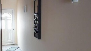 Un pasillo con techo de madera, una obra de arte enmarcada, una lámpara blanca fijada a la pared y una puerta al final.