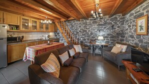 A cozy interior with wooden beams, a stone wall, a sofa, a dining table, and a kitchen area.