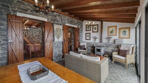 A rustic interior with stone walls, wooden beams, wicker furniture, and a fireplace.