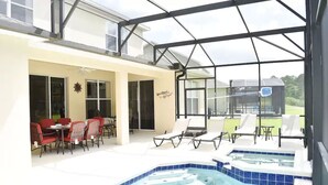 A covered outdoor area with a pool, lounge chairs, and a dining table with red chairs. - Spacious Luxurious 6 Bedroom 5 Bath Villa Sleeps 12 Pool, Jacuzzi, near Disney (Kissimmee)