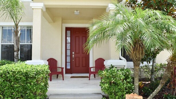 A house with a red door, two red chairs, and a welcome sign. - Spacious Luxurious 6 Bedroom 5 Bath Villa Sleeps 12 Pool, Jacuzzi, near Disney (Kissimmee)