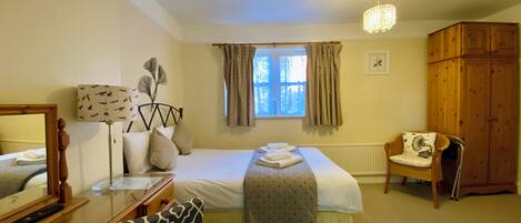 A bedroom with a bed, a desk, a chair, a wardrobe, and a window with curtains.