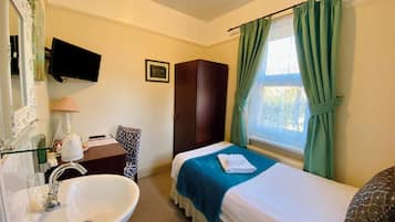 Een hotelkamer met een bed, een bureau met lamp, een spiegel, een wastafel en een raam met gordijnen.