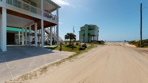 A coastal building with a balcony, a dirt road, and a beach in the background. - Salty Waves: 3  BR, 2  BA House in Port Bolivar, Sleeps 12 (Bolivar Peninsula)