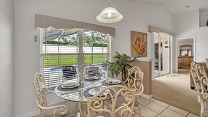A dining area with a glass table and metal chairs, a hanging light fixture, and a view of a green landscape through a window with blinds. - No Rear Neighbors, Near Disney Spacious Home With CDC Standards #3hr836 (Davenport)