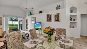 A dining area with a glass table, chairs, and a TV in the background. - No Rear Neighbors, Near Disney Spacious Home With CDC Standards #3hr836 (Davenport)