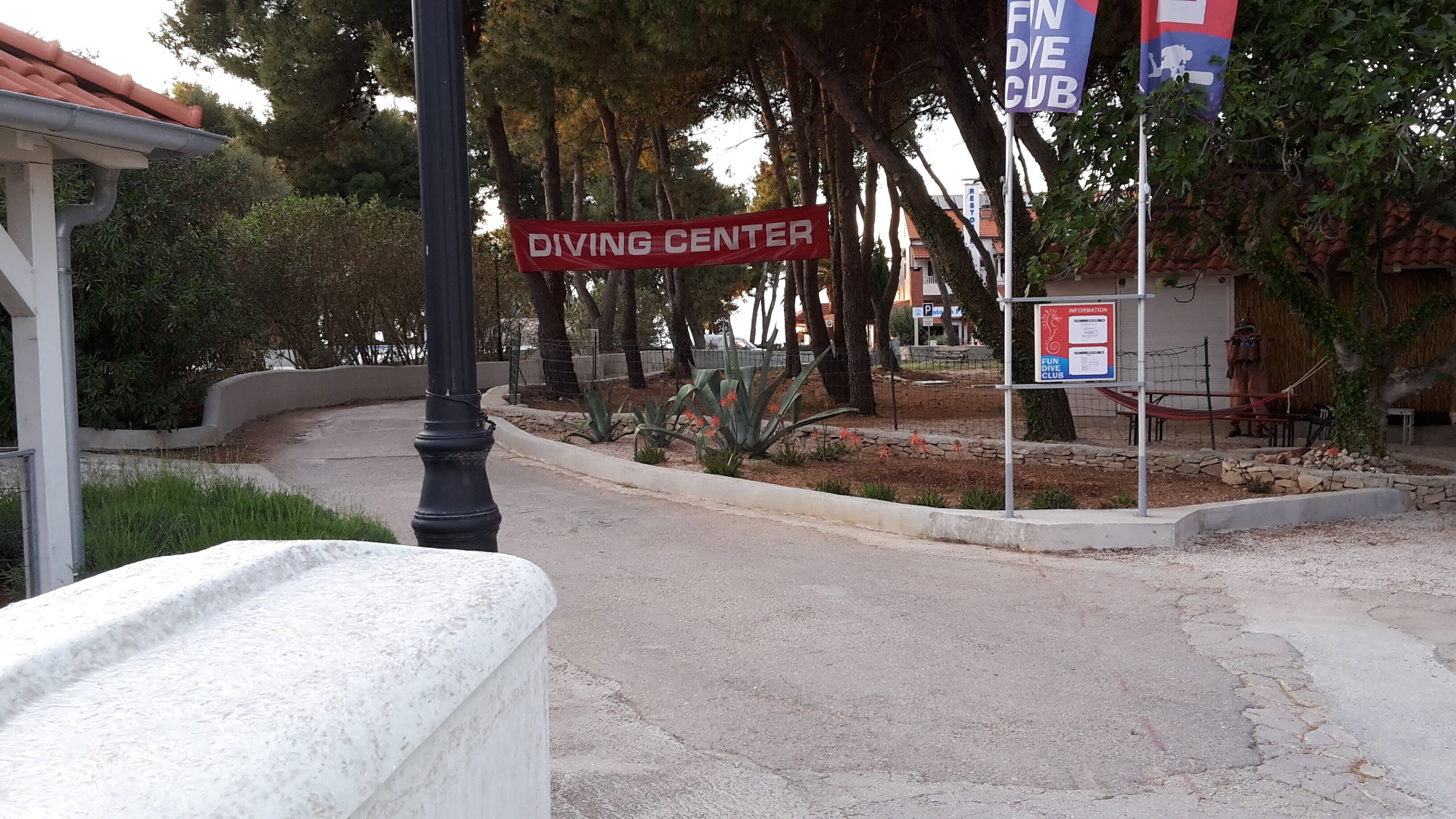 A street sign for a Diving Center, a fenced area with trees, and a building with a red roof.