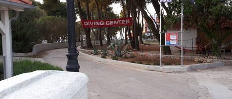 A street sign for a Diving Center, a fenced area with trees, and a building with a red roof.