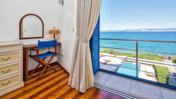 A room with a wooden floor, a desk with a chair, a mirror, a lamp, and a large window with a view of the sea and a pool. - Beachfront twin villa, private heated pools and amazing sea views - Villa Violet (Supetar)