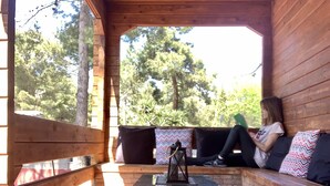 A wooden deck with a glass table and benches, surrounded by trees.