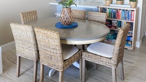 A dining area with wicker chairs, a round table, and a hanging light fixture.