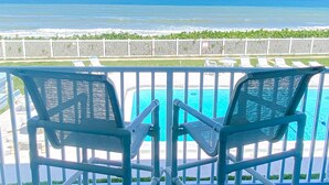 Two chairs facing a pool with a view of the ocean.