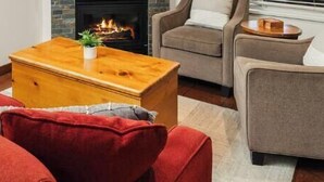 A living room with a red sofa, a beige armchair, a wooden coffee table, and a fireplace.