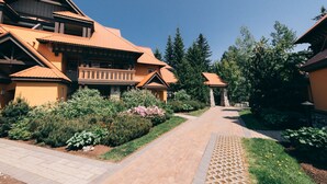 A traditional lodge with a central pathway, surrounded by lush greenery and tall trees.