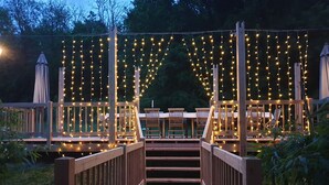 Une terrasse en bois dotée d’une rambarde, de guirlandes lumineuses et de mobilier d’extérieur.