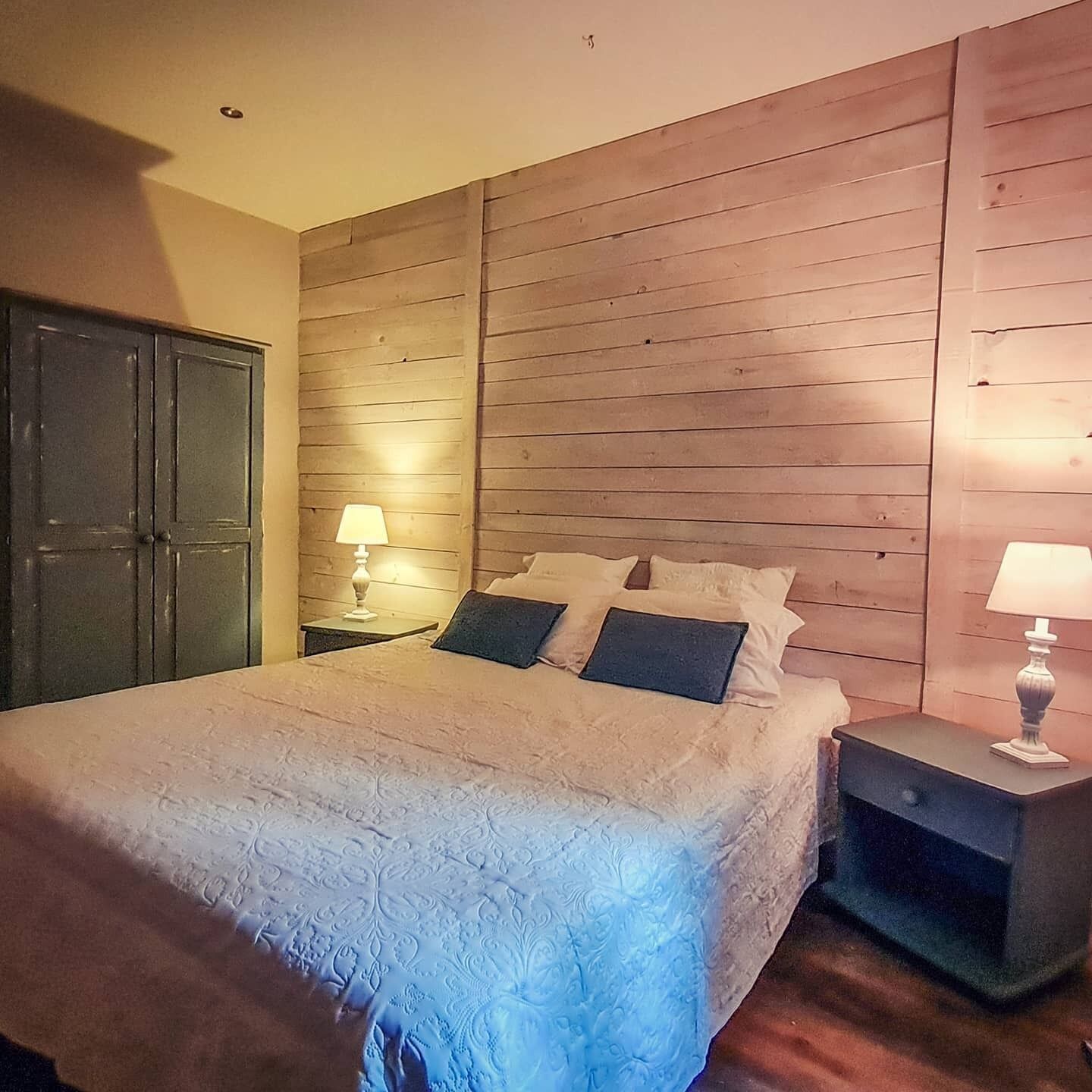 Une chambre à coucher avec un grand lit, des lambris en bois sur les murs, deux tables de chevet avec des lampes et une armoire.