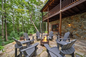 An outdoor seating area with Adirondack chairs around a fire pit, set against a stone wall and surrounded by trees.