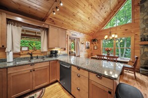 A wooden cabin interior with a kitchen, dining area, and a stone fireplace.