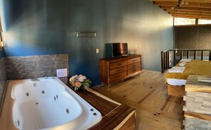 A modern bathroom with a large bathtub, wooden vanity, and a television on a wooden dresser.