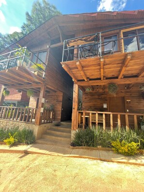 A wooden cabin with a balcony, a porch, and a staircase leading to the entrance.