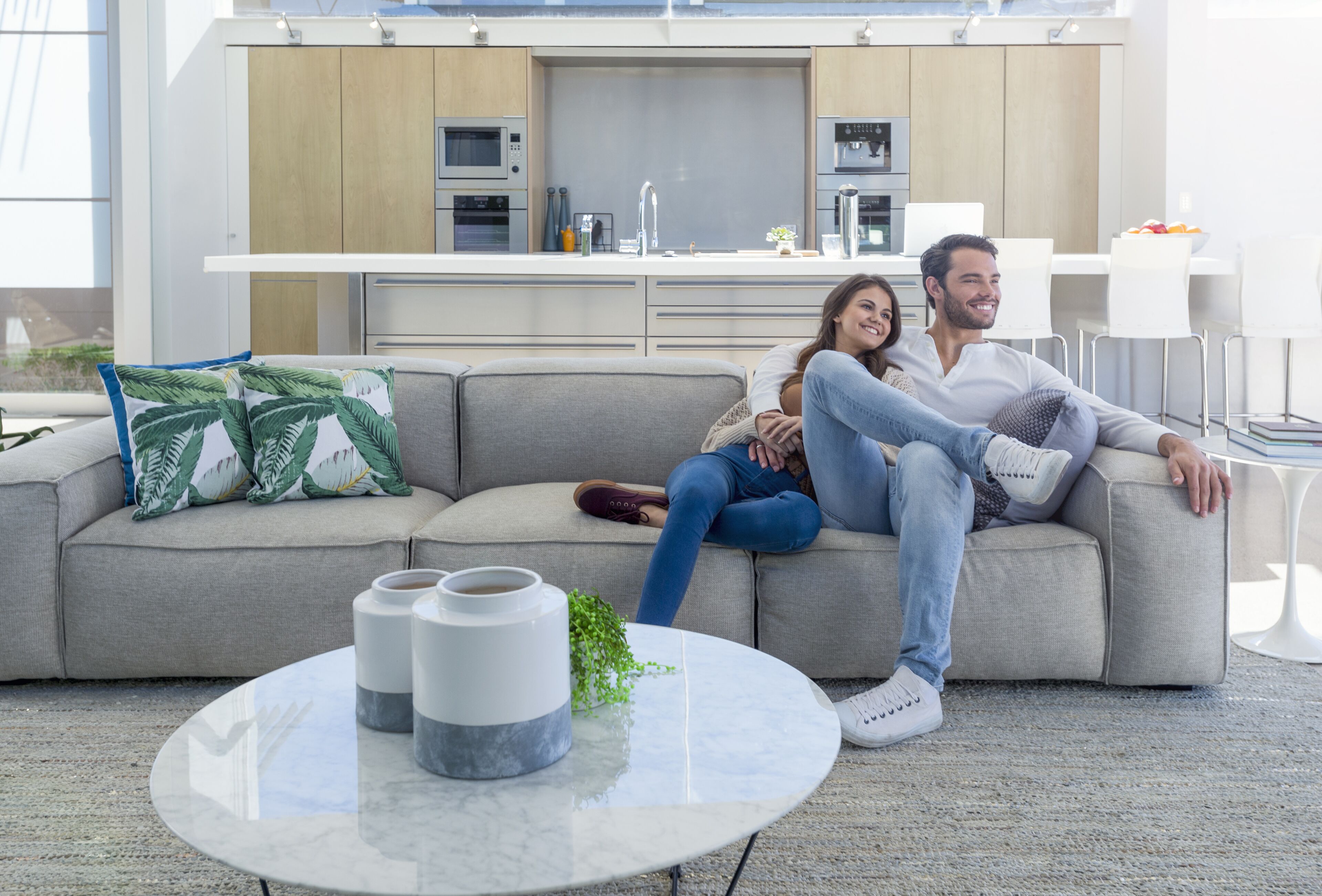 En moderne stue med sofa, sofabord og et køkken i baggrunden.