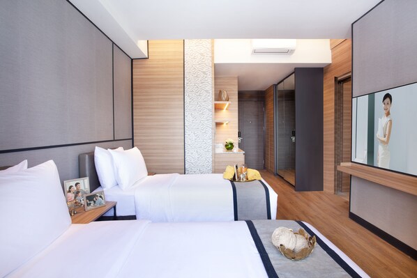 Une chambre d’hôtel avec deux lits, une télévision, une petite table avec un bol et un cadre photo, et une salle de bain visible à travers une porte en verre.