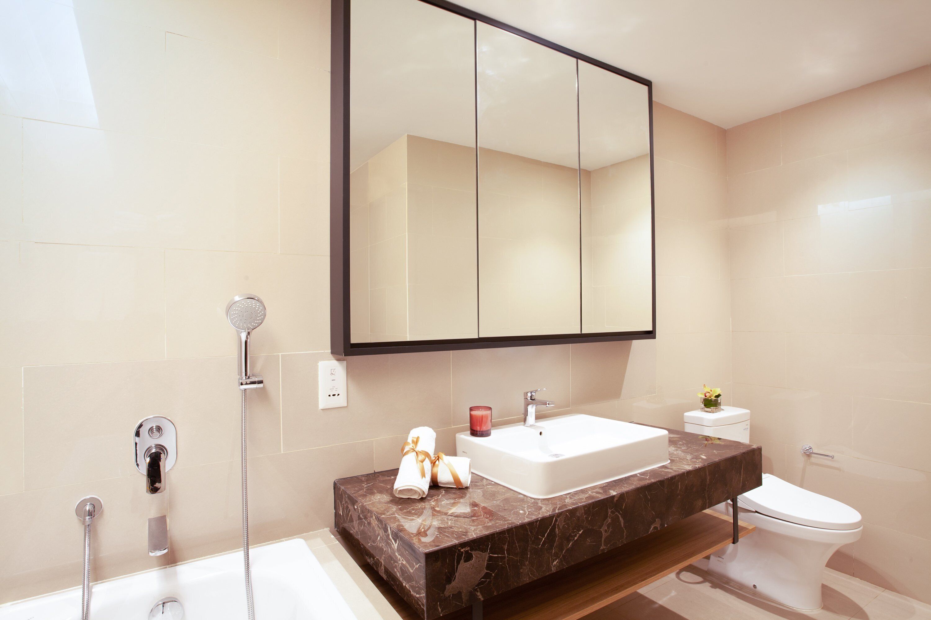 A modern bathroom with a large mirror, a bathtub, a sink, and a toilet.