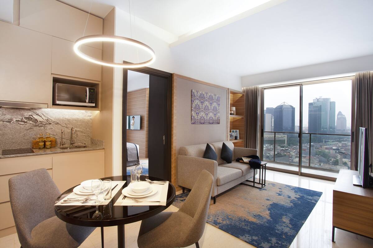Una habitación de hotel moderna con zona de comedor, sofá y un amplio ventanal con vistas a la ciudad.
