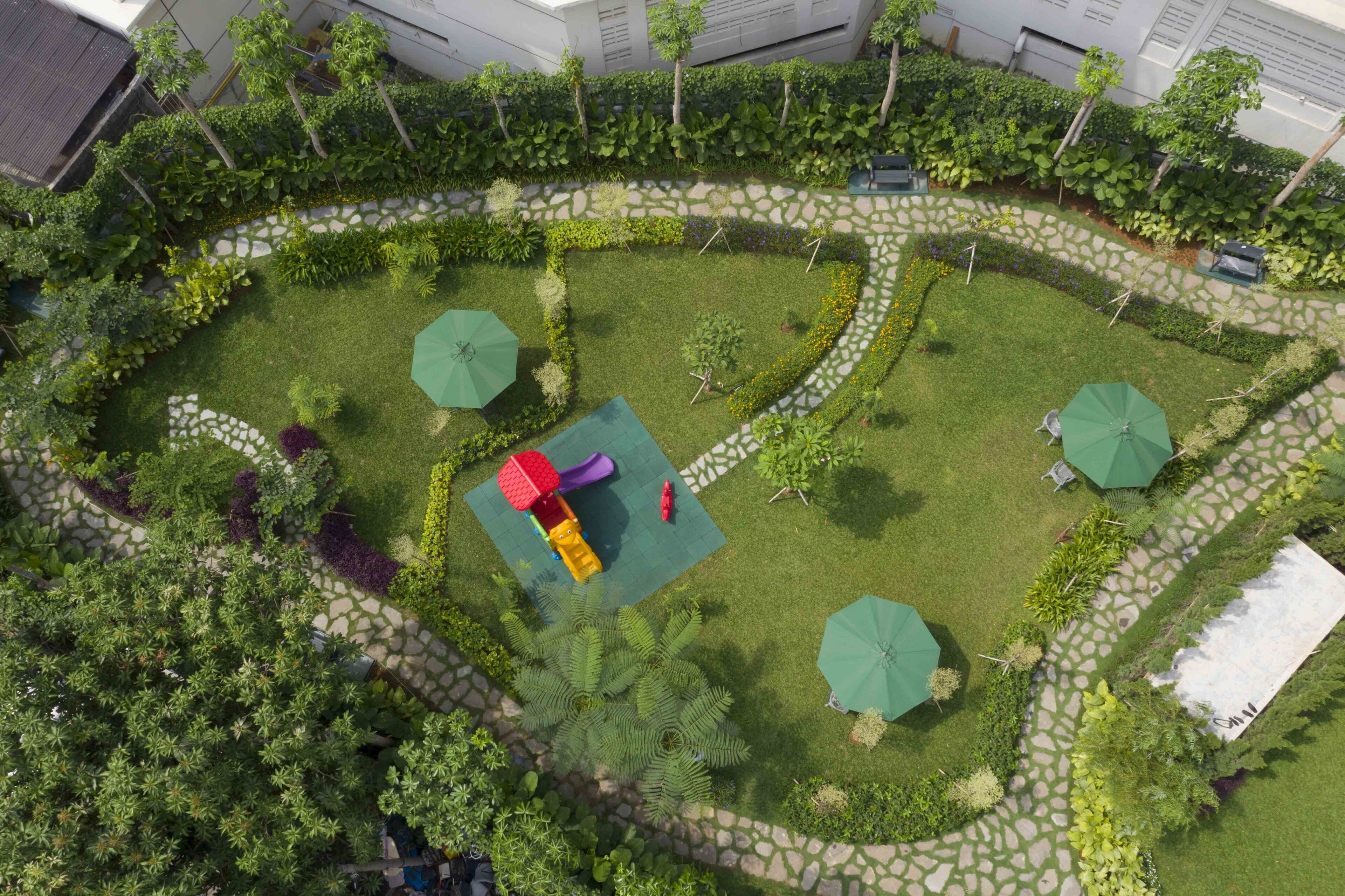 An aerial view of a landscaped garden with a children's play area, stone pathways, and green umbrellas.