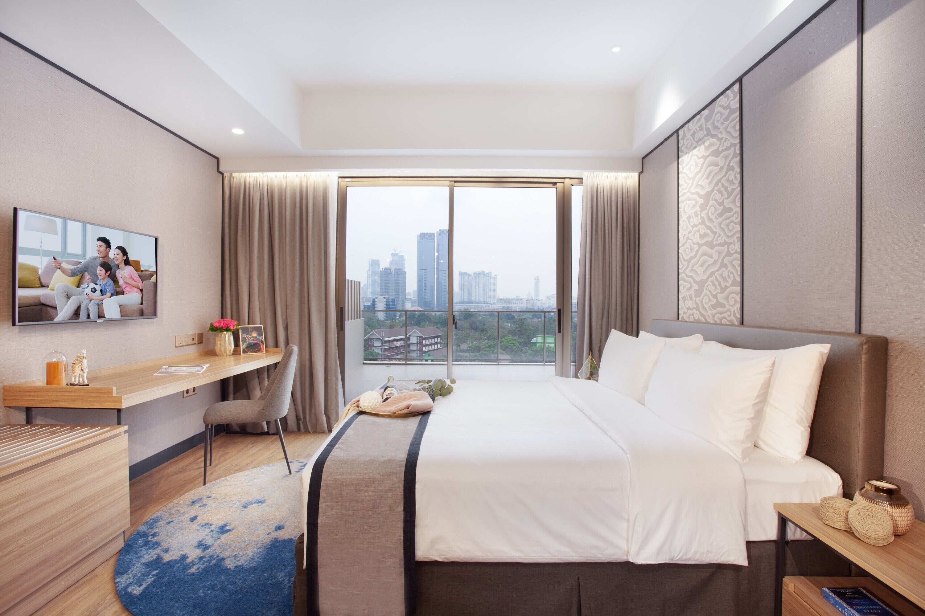 A modern hotel room with a large bed, a desk, a chair, a TV, and a city view.