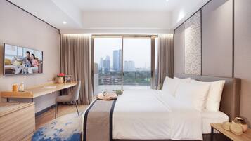 Ein modernes Hotelzimmer mit einem großen Bett, einem Schreibtisch, einem Stuhl, einem Fernseher und Blick auf die Stadt.