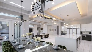 A modern kitchen with a central island, built-in appliances, and a dining area with a long table set for six. - The Modern Jewel | 10BR Luxury Estate w/ Themed Rooms, Private Pool, Arcade, and Theater Near Disney (Kissimmee)