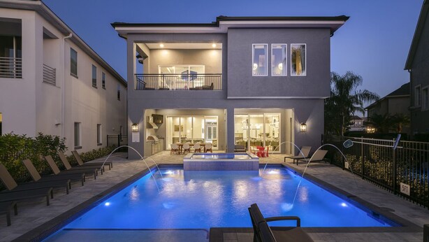 A modern two-story house with a swimming pool, outdoor seating, and a well-lit interior. - The Modern Jewel | 10BR Luxury Estate w/ Themed Rooms, Private Pool, Arcade, and Theater Near Disney (Kissimmee)