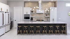 Une cuisine moderne dotée d’un îlot central, de meubles blancs, d’un pare-feu en pierre et d’un luminaire suspendu.