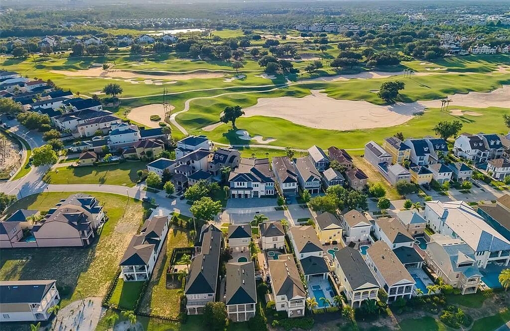 An aerial view of a residential area with houses, a golf course, and a road.