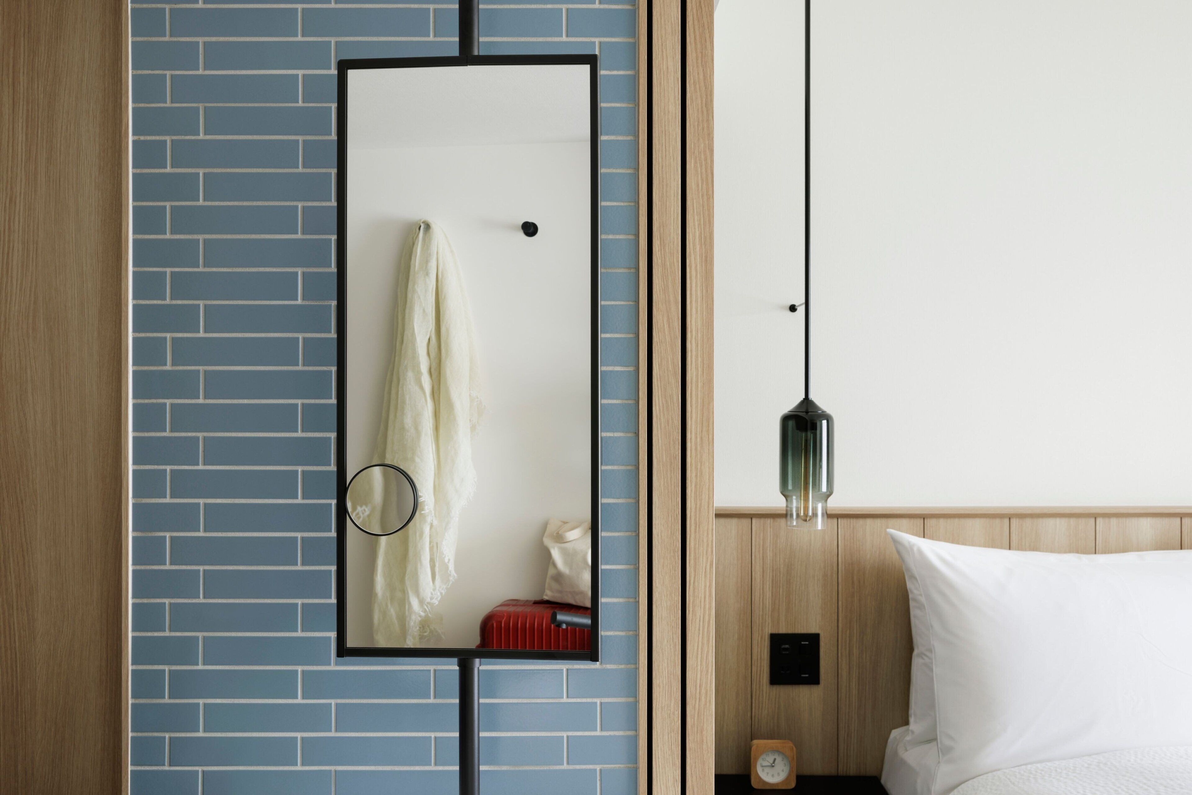 Une chambre d’hôtel avec un mur en briques bleues, une tête de lit en bois, un lit avec une literie blanche, une table de chevet avec une horloge et une lampe suspendue.