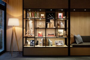A modern interior with a wooden bookshelf displaying various items, a floor lamp, and a sofa with cushions.