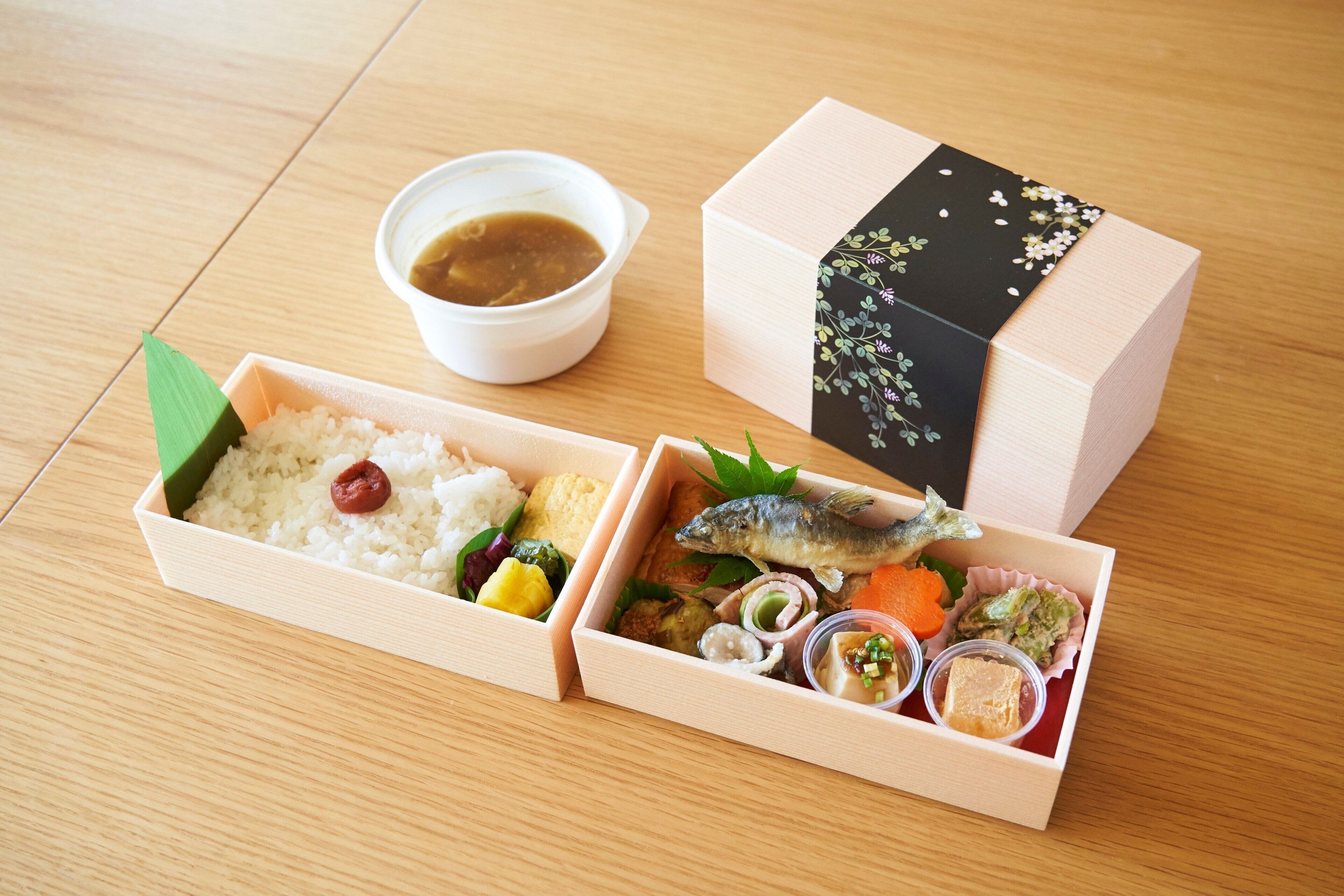 Two wooden boxes with food items, one containing rice and vegetables, and the other with fish and sauces.