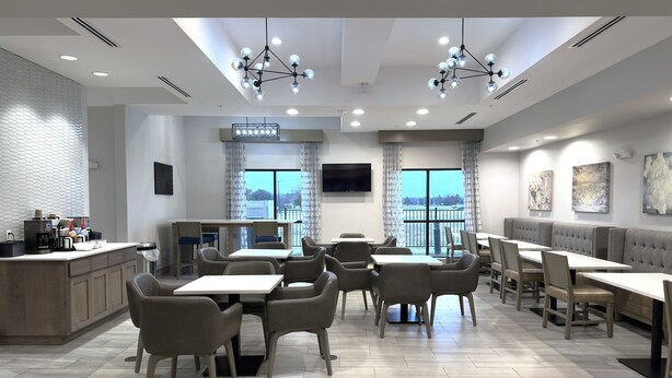 A modern dining area with a kitchen counter, seating arrangements, and a large window with a view. - Merica Inn & Suites (Wills Point)
