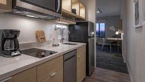 A modern kitchen with a built-in microwave, coffee maker, and dishwasher. There is a dining area with a table and chairs visible in the background. - TownePlace Suites by Marriott Wrentham Plainville (Plainville)