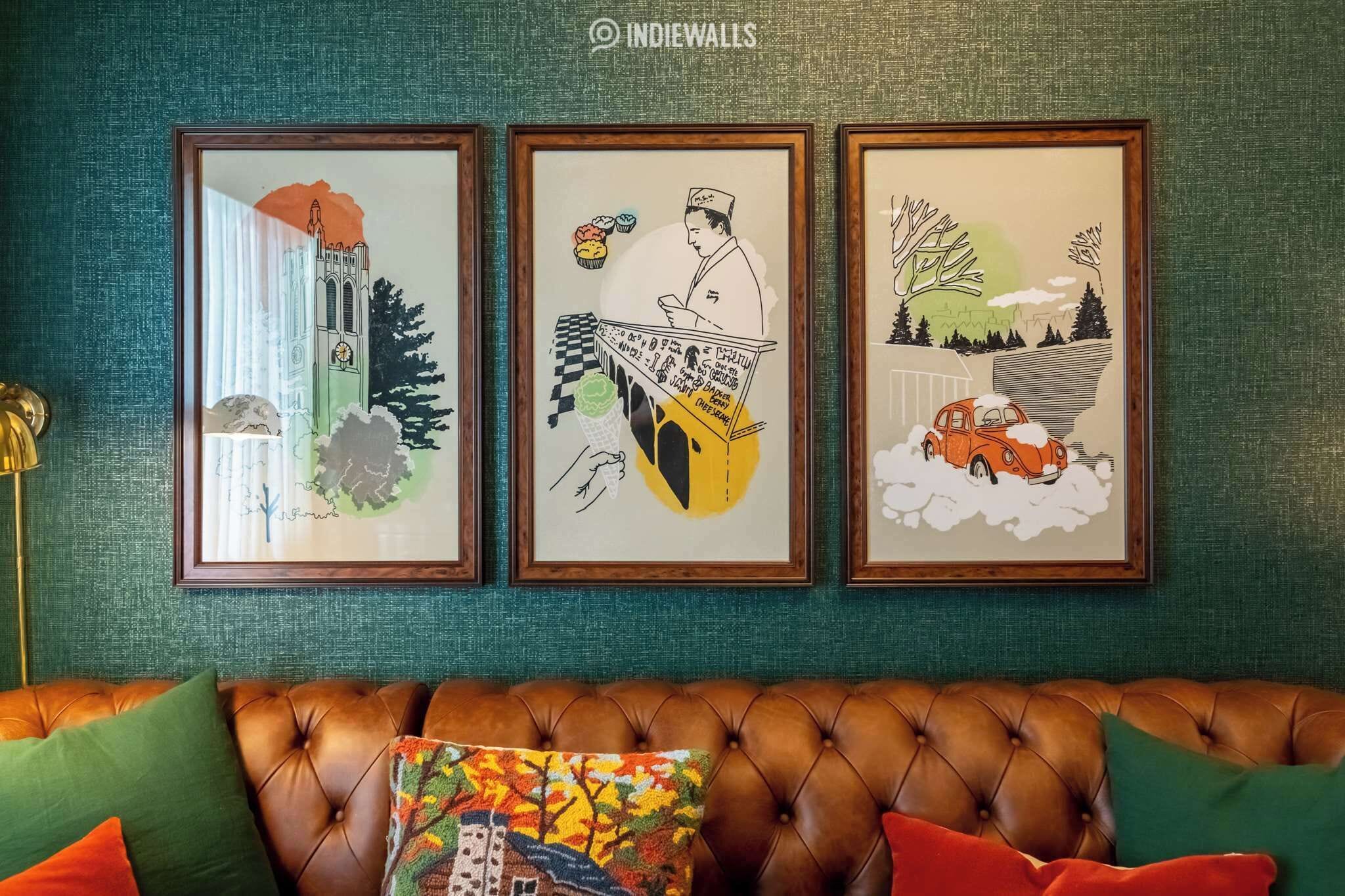 Three framed artworks on a teal wall, a brown leather couch with colorful cushions, and a gold floor lamp.