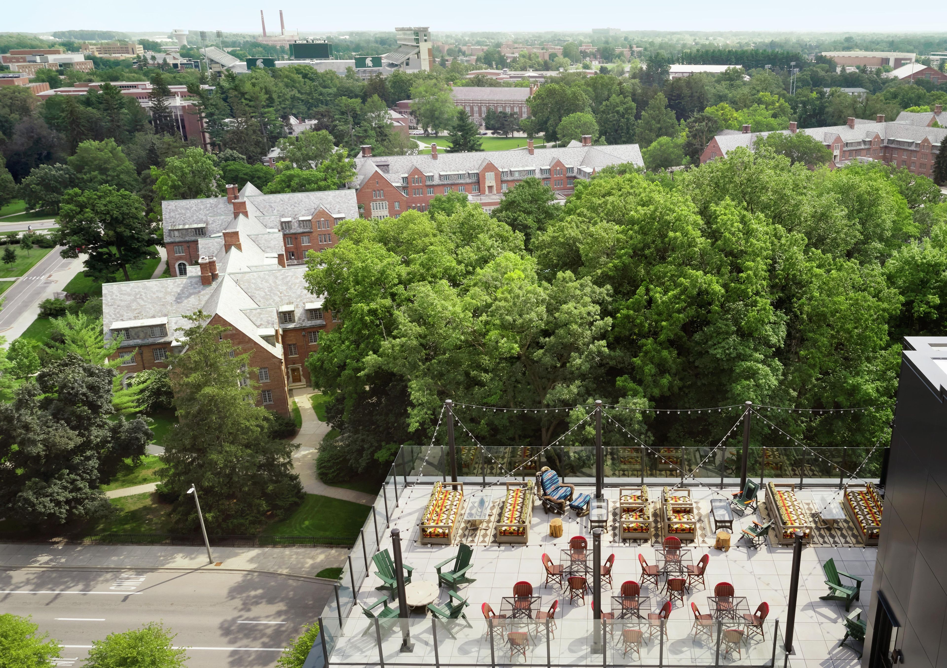 A rooftop terrace with outdoor seating and a view of a campus.