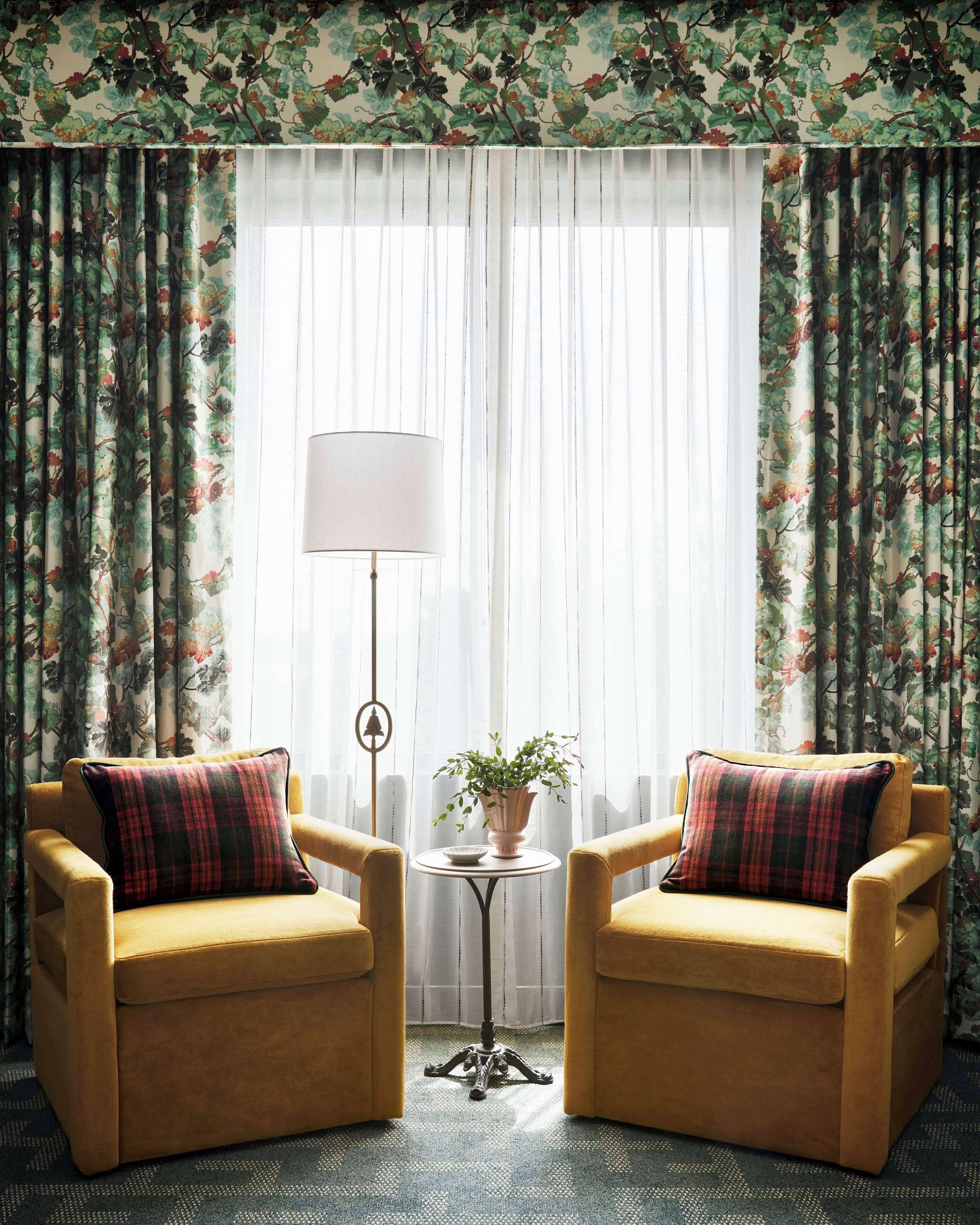 A room with two armchairs, a floor lamp, a small table with a plant, and floral wallpaper.