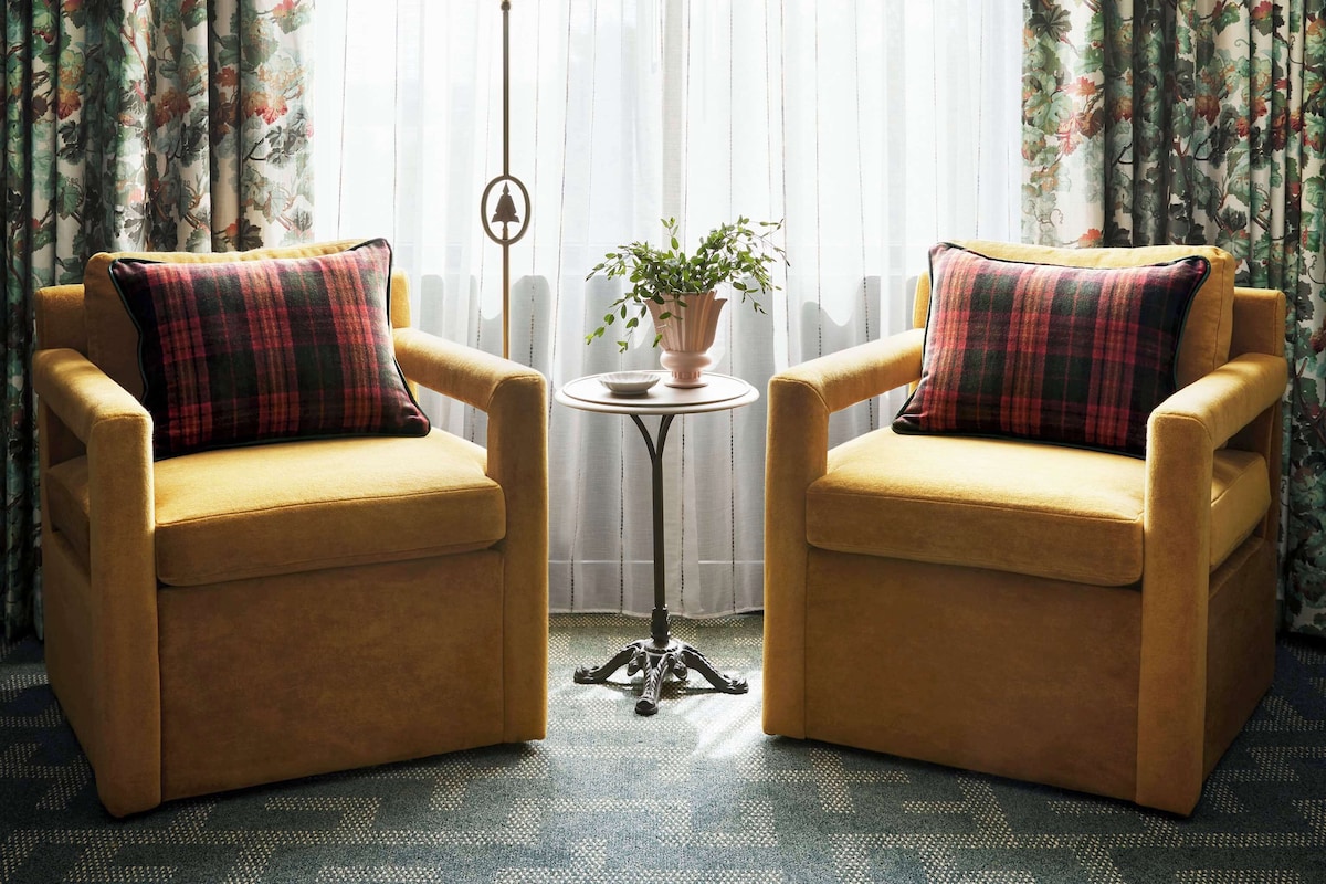 A room with two armchairs, a floor lamp, a small table with a plant, and floral wallpaper.